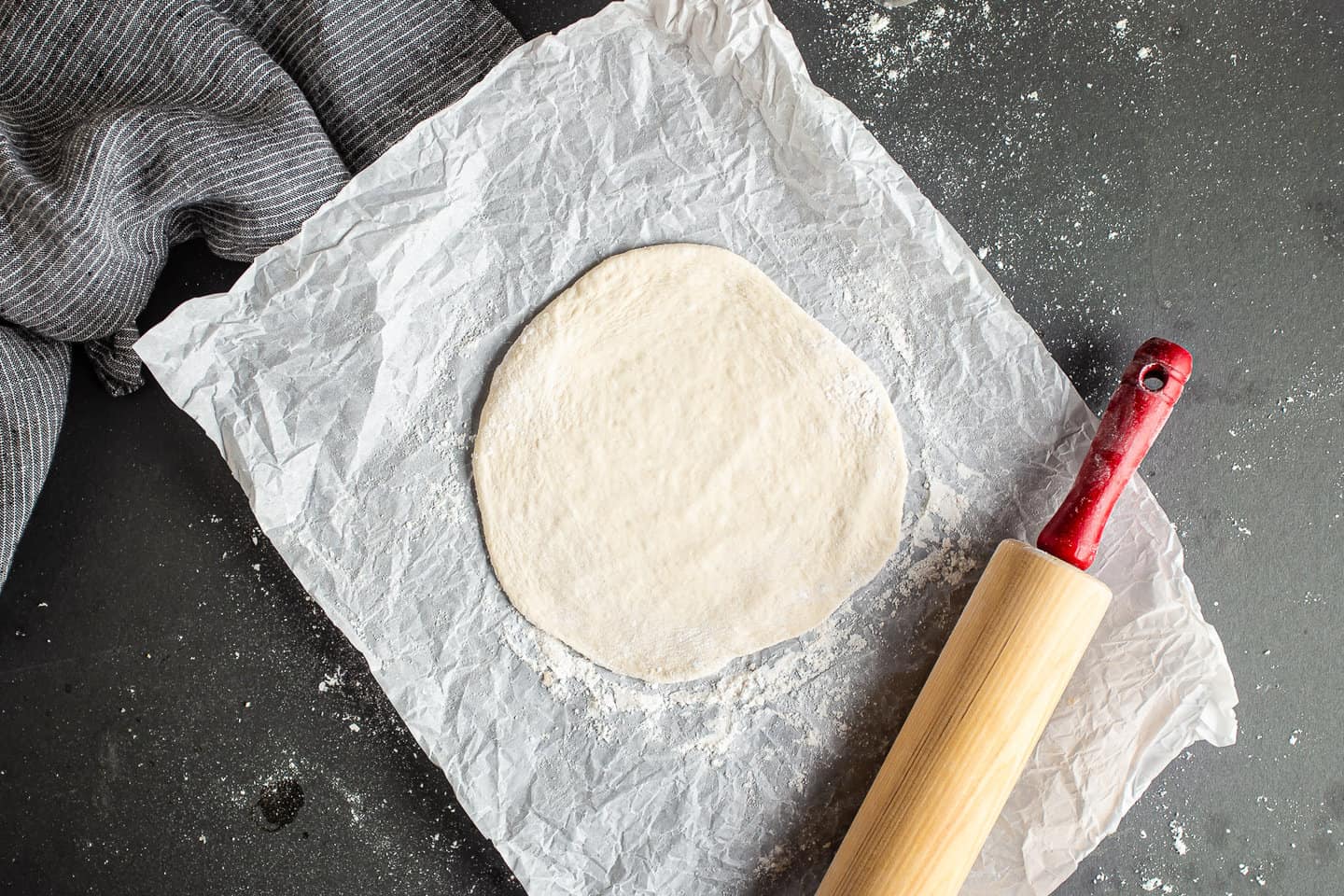 Rolling pita bread dough into flat circles with a rolling pin.