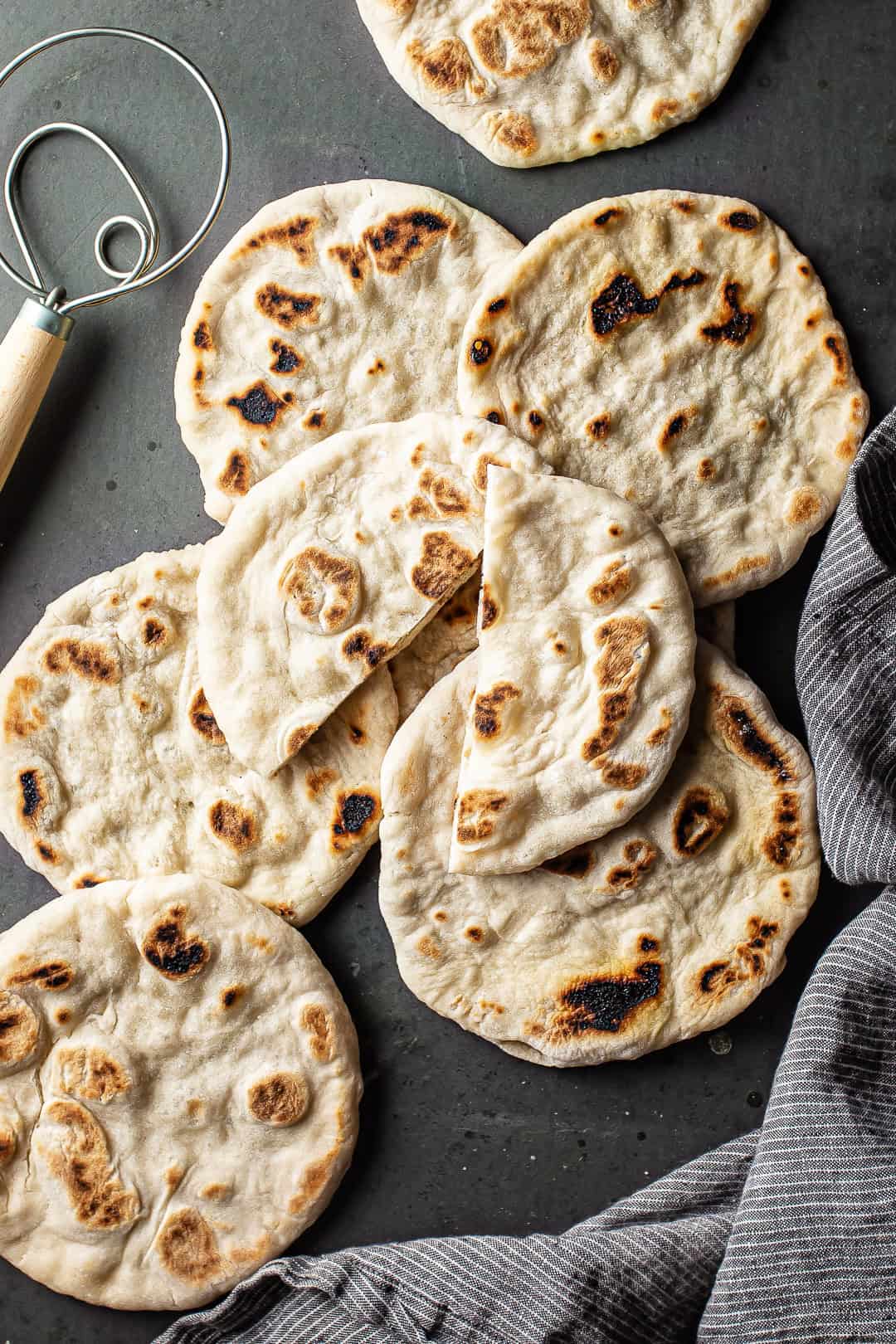 Pita bread recipe, prepared and cooked and displayed on a dark background with a striped kitchen cloth.
