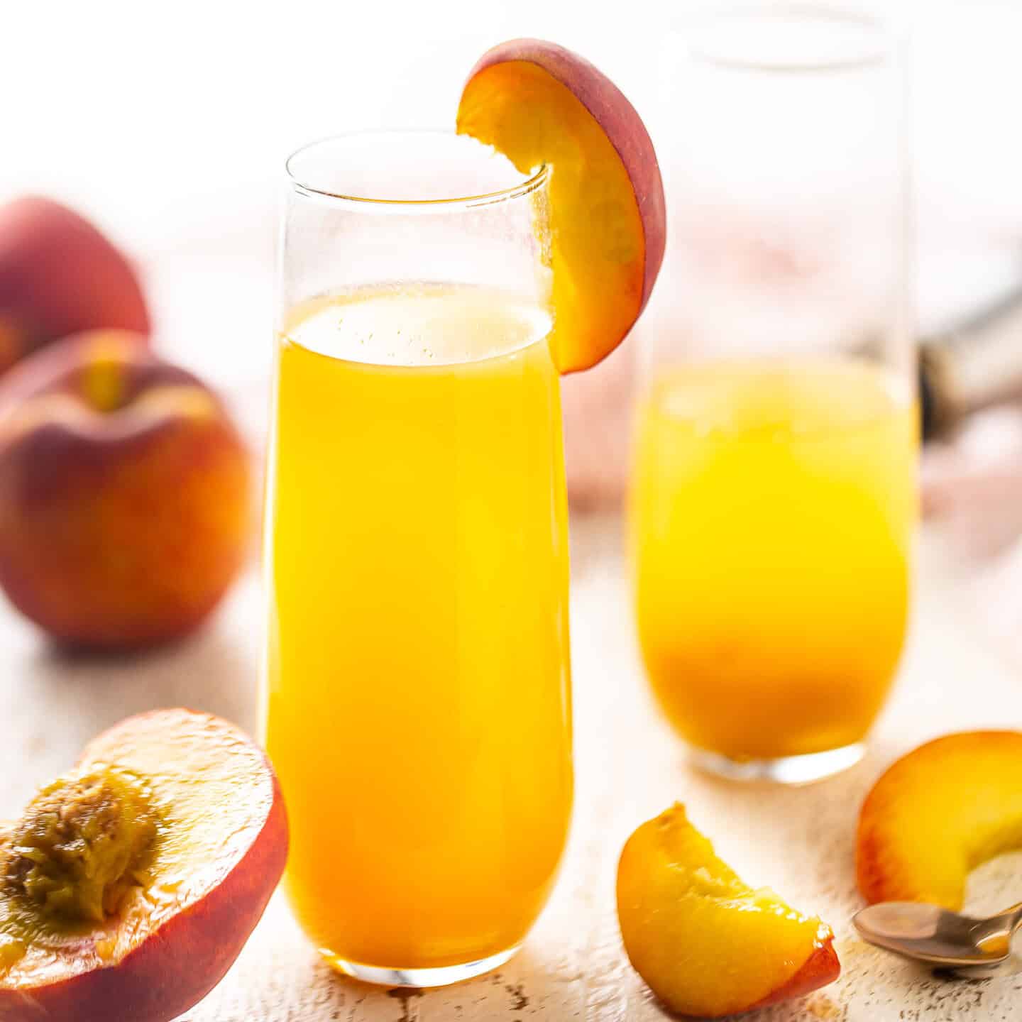 Bellini drink in a champagne flute with a wedge of fresh peach.
