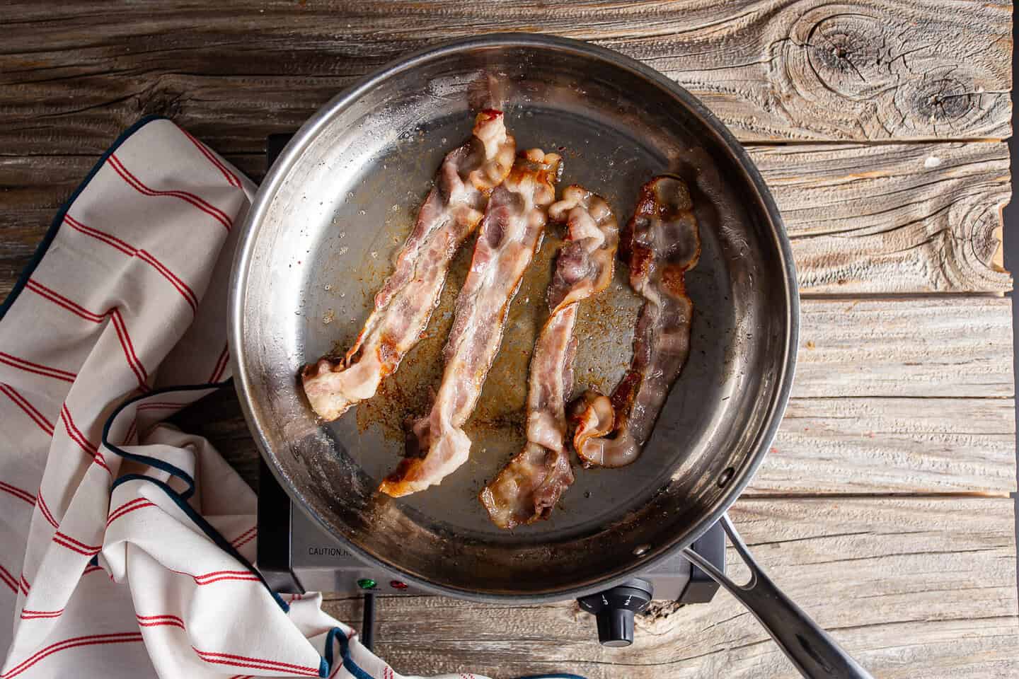 Rendering bacon in a large stainless steel skillet.