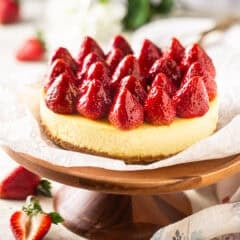 Strawberry cheesecake on a wooden cake pedestal.