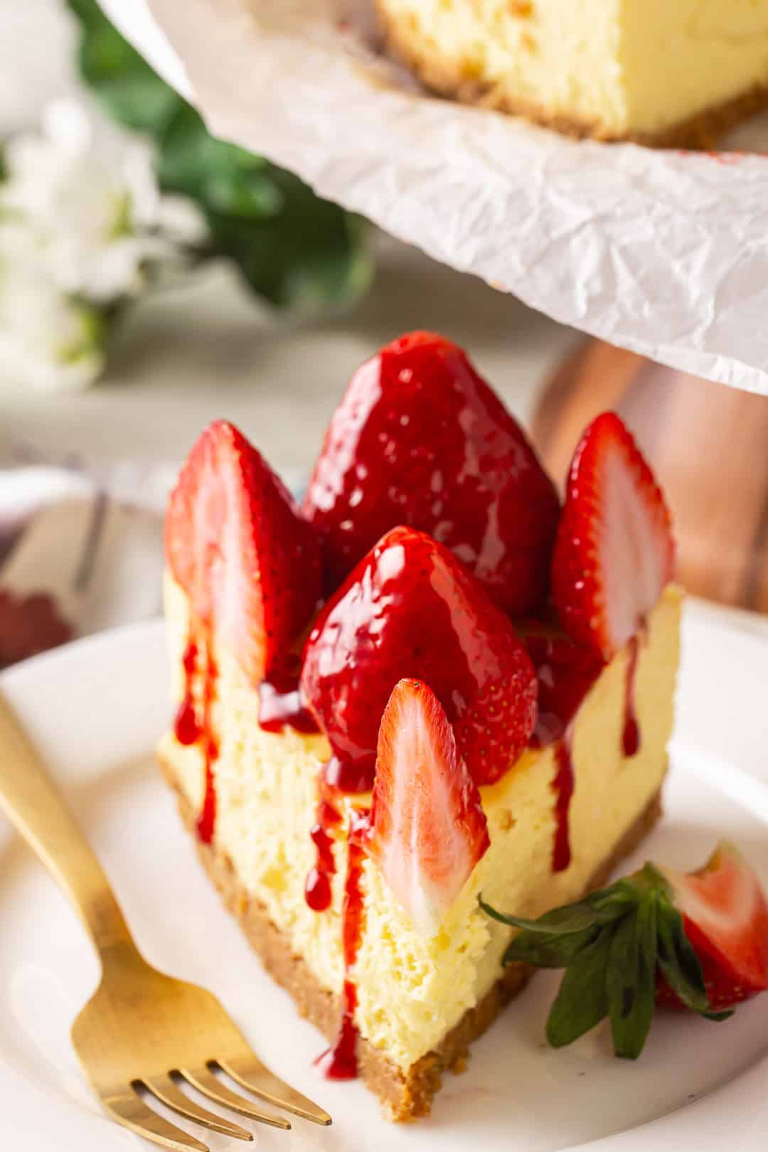 Cheesecake and strawberry on a white plate with a gold fork.