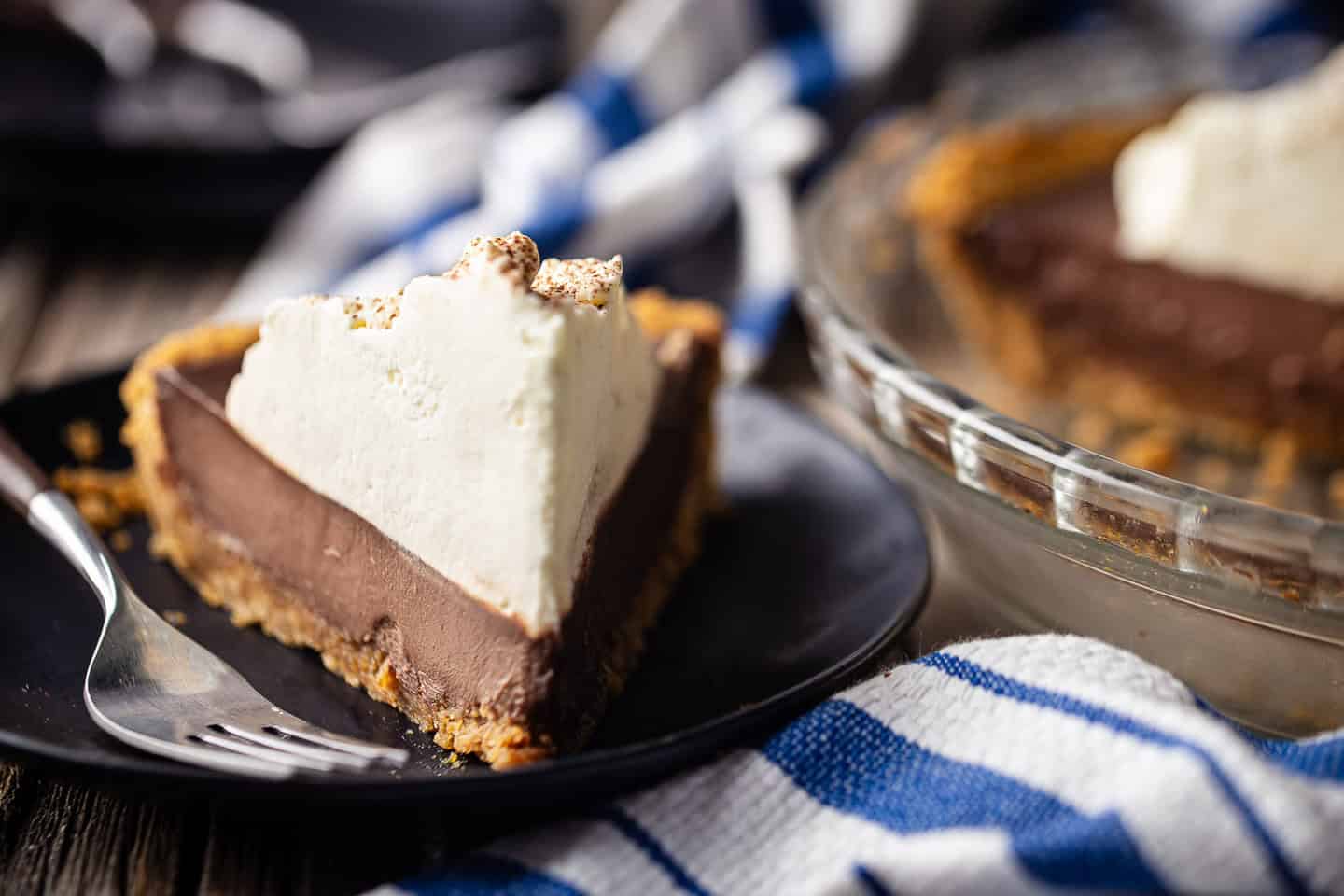Chocolate pudding pie with Graham cracker crust, sliced and served on a dark blue plate.
