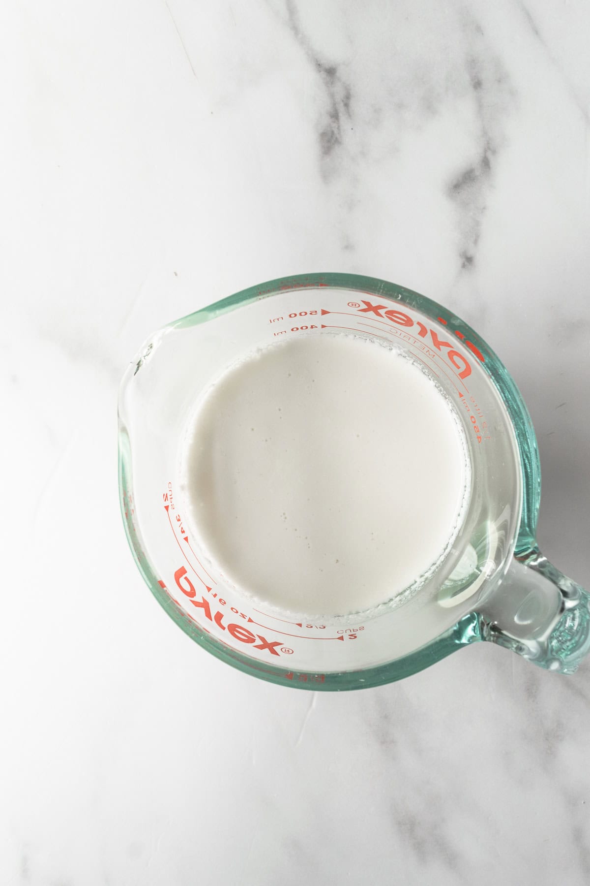 homemade buttermilk in a glass measuring cup on a white table.