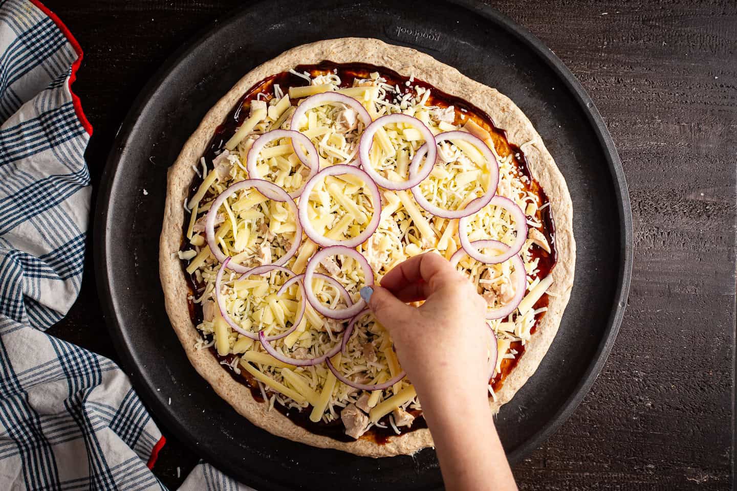 Topping homemade pizza with cooked chicken, cheese, and thin slices of red onion.