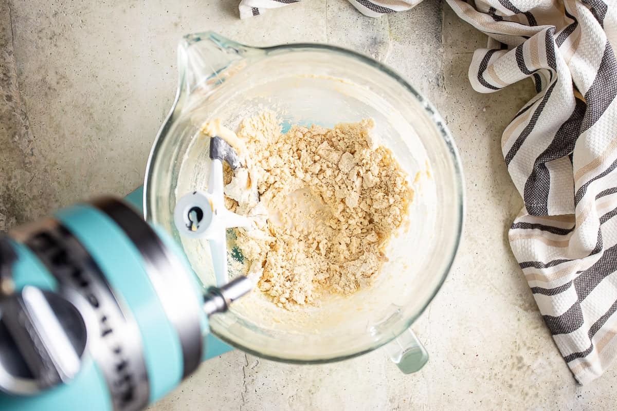 Crumbly edible cookie dough in the bowl of a stand mixer.