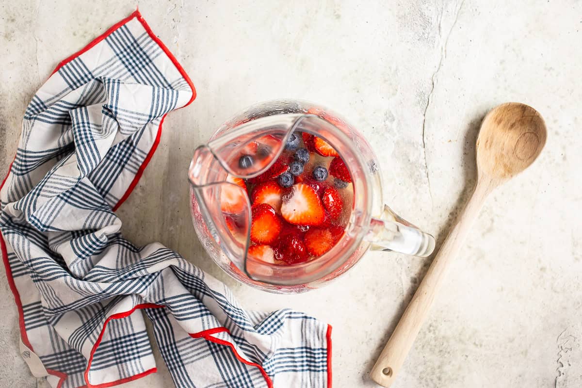 Adding berries to a pitcher of white sangria.