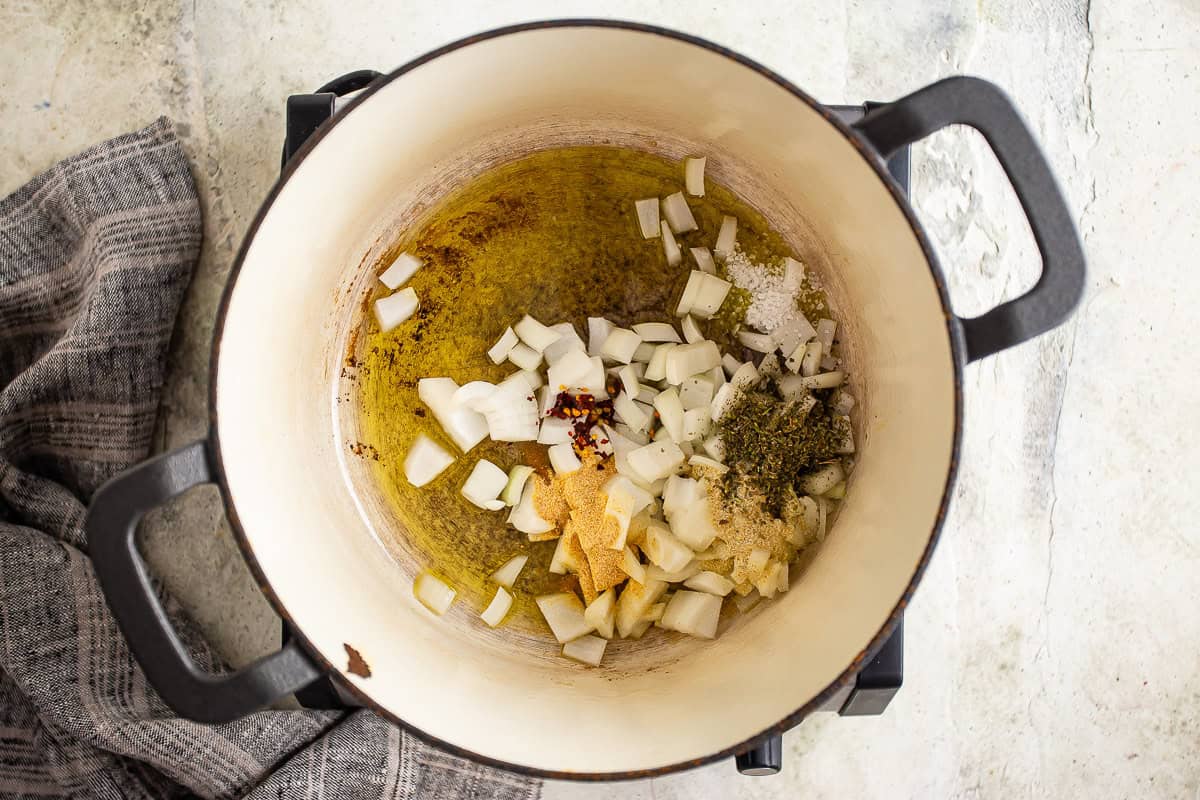 Olive oil, onions, and seasonings in a large enameled cast iron pot.