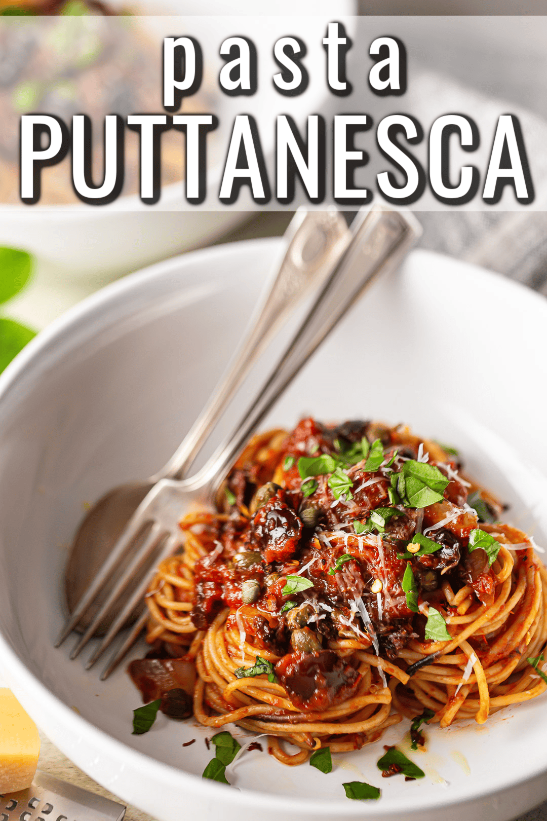 Pasta puttanesca served in a white bowl with torn fresh basil.