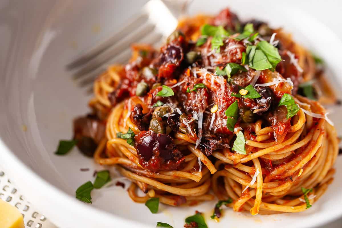 Close-up image of spaghetti puttanesca recipe, featuring black olives and capers.