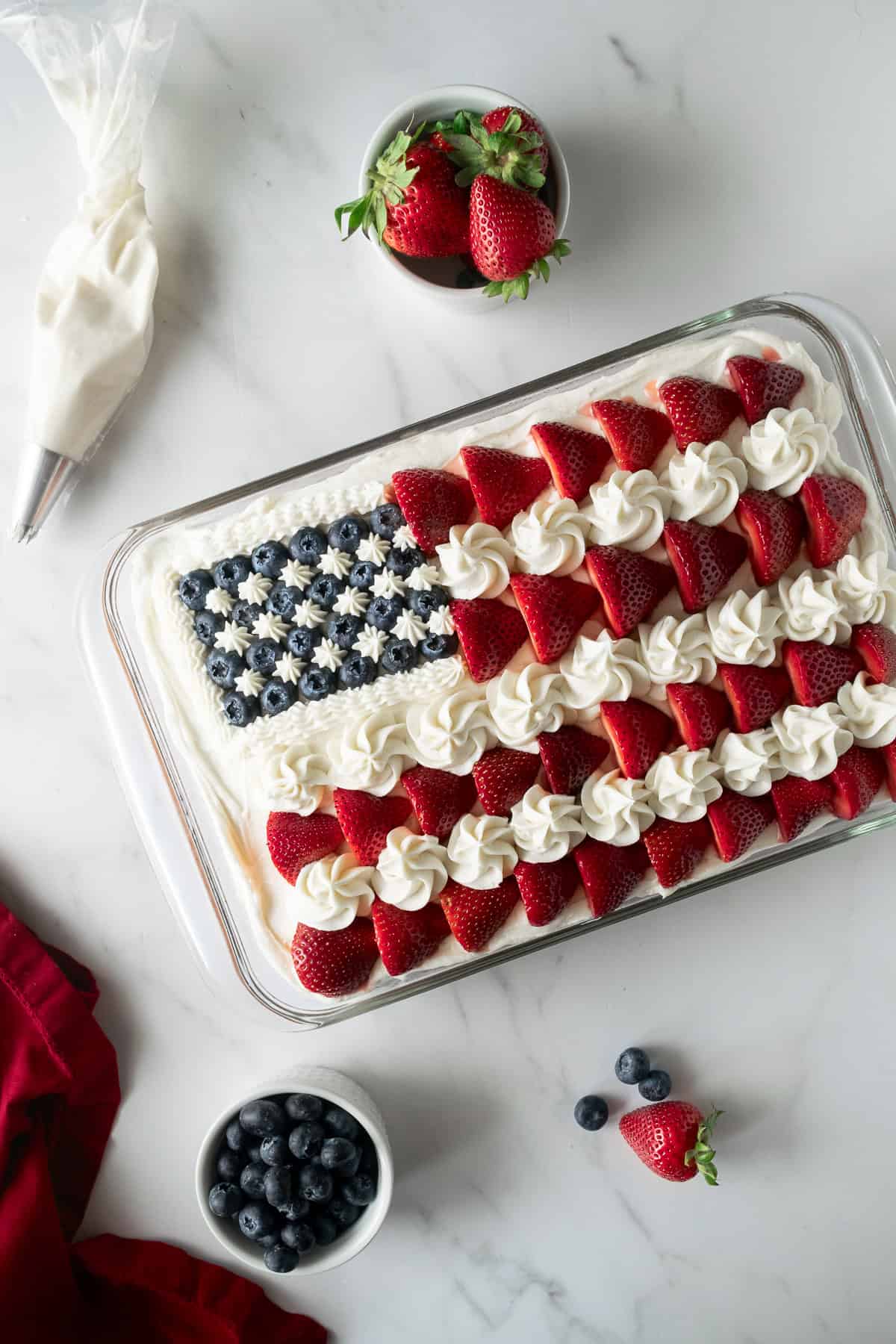 american flag cake in a baking pan topped with vanilla frosting, strawberries, and blueberries.