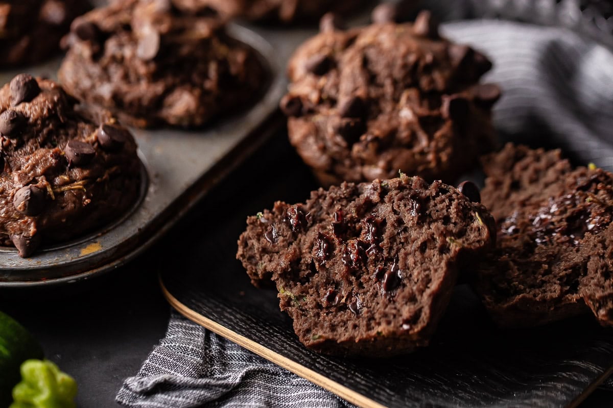 A chocolate zucchini muffin split vertically to show off its shape and all the pockets of melted chocolate running throughout.