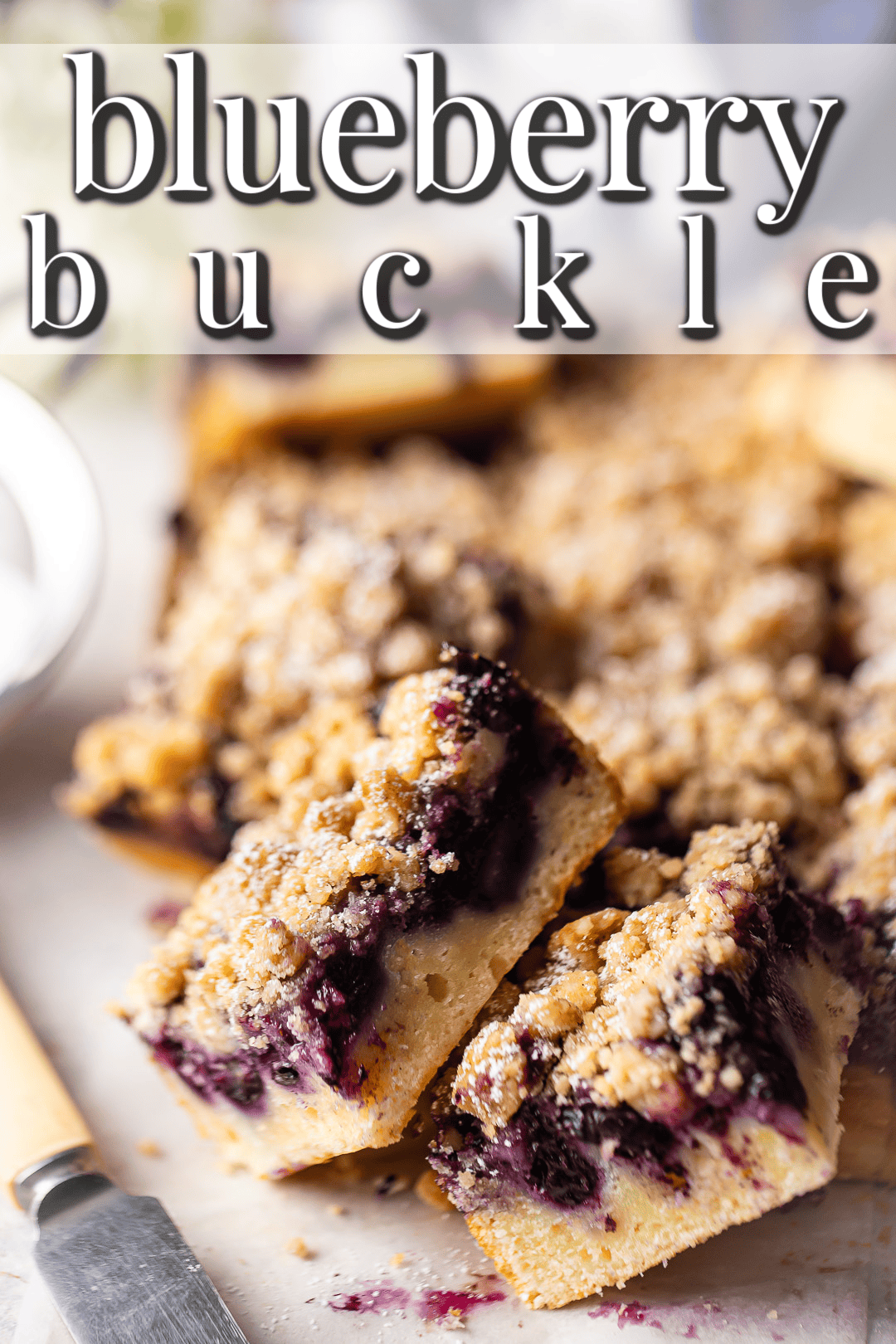 Squares of blueberry buckle in a pile with a text banner above that reads "Blueberry Buckle."