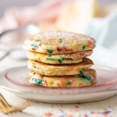 A stack of funfetti pancakes on a pink glass plate.