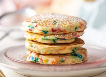 A stack of funfetti pancakes on a pink glass plate.