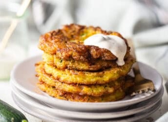 Zucchini fritters stacked on a plate with a creamy sauce on top.