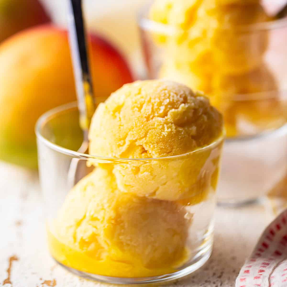 Two scoops of mango sorbet in a small glass dish with a spoon.