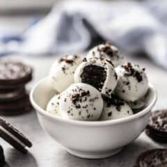 oreo balls in a white bowl coated in white chocolate and sprinkled with oreo crumbs.
