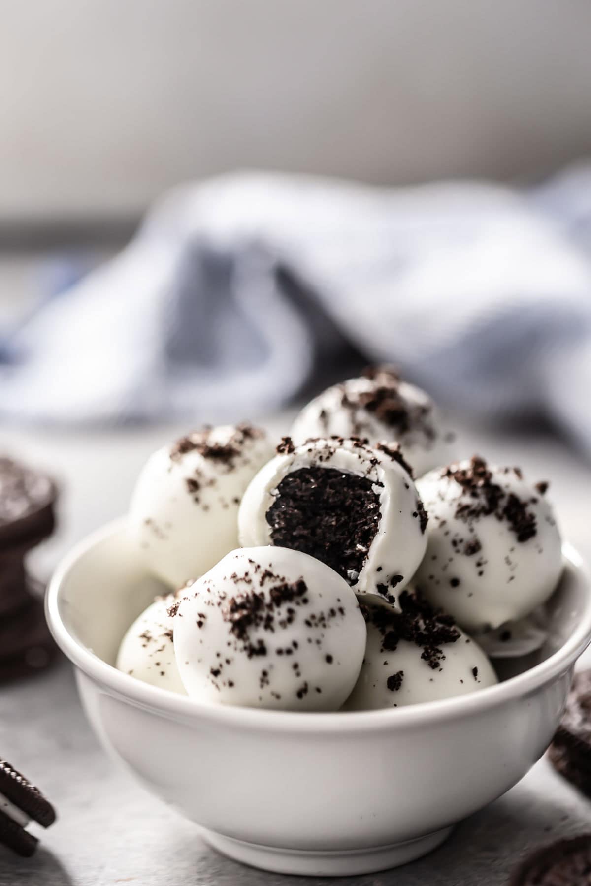 oreo truffle balls in a bowl coated in white chocolate with a bite taken from it and sprinkled with oreo crumbs.