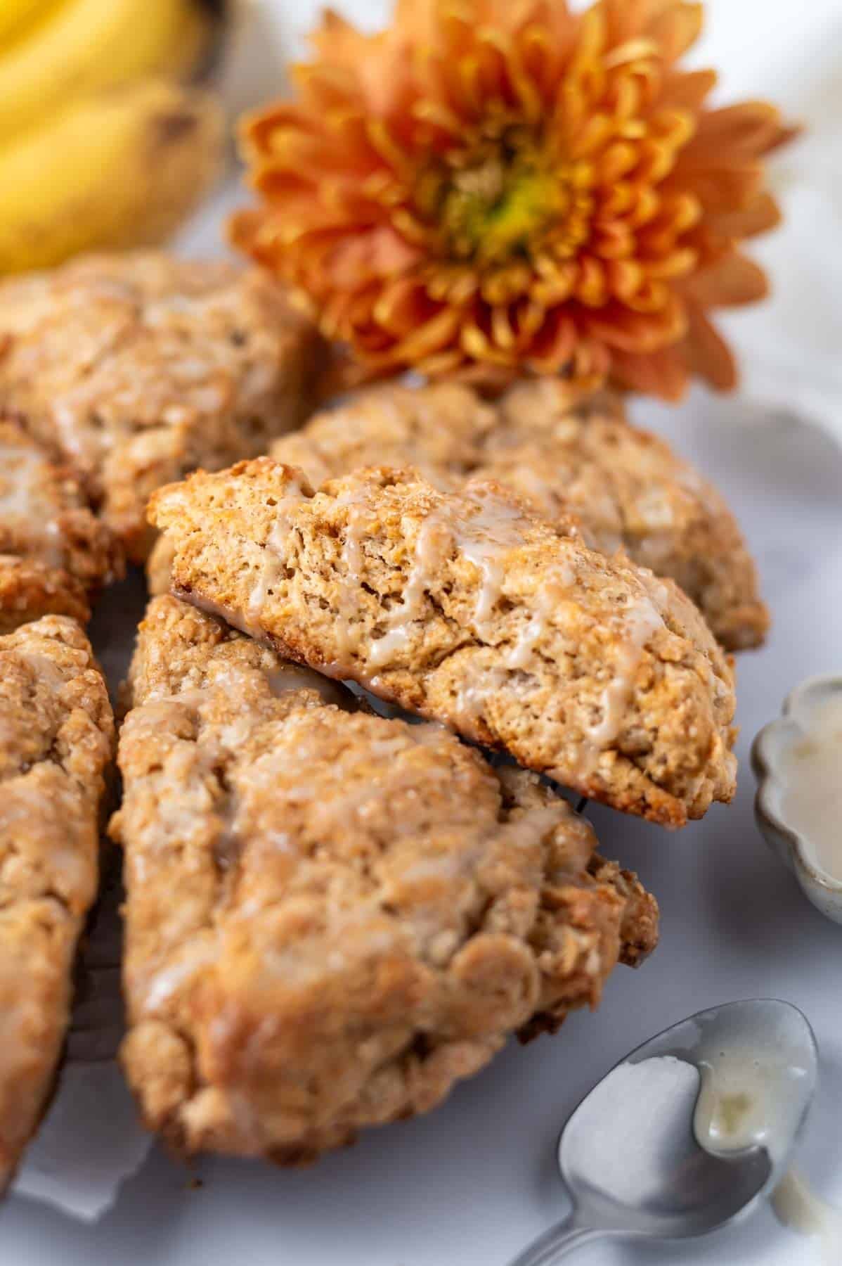 banana scones with a banana icing on parchment paper with fresh flower and ripe bananas in the background