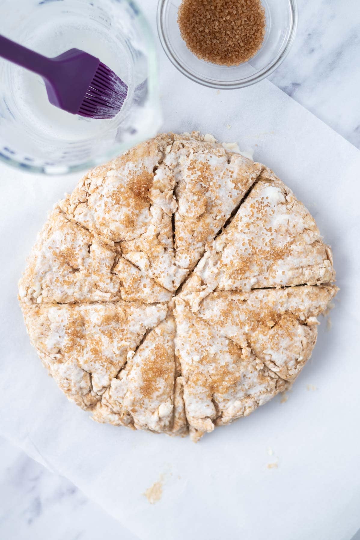 over head look a scone dough cut into triangles with heavy cream and turbinado sugar on the top