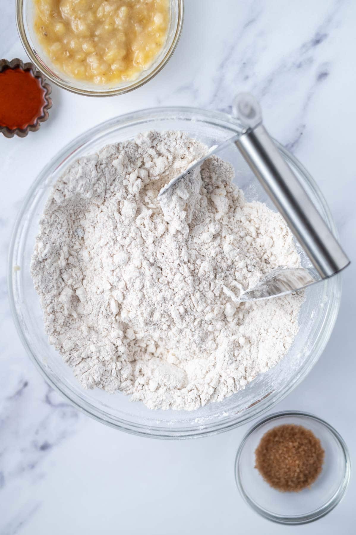 grated butter worked into flour mixture in a glass bowl with a pastry cutter