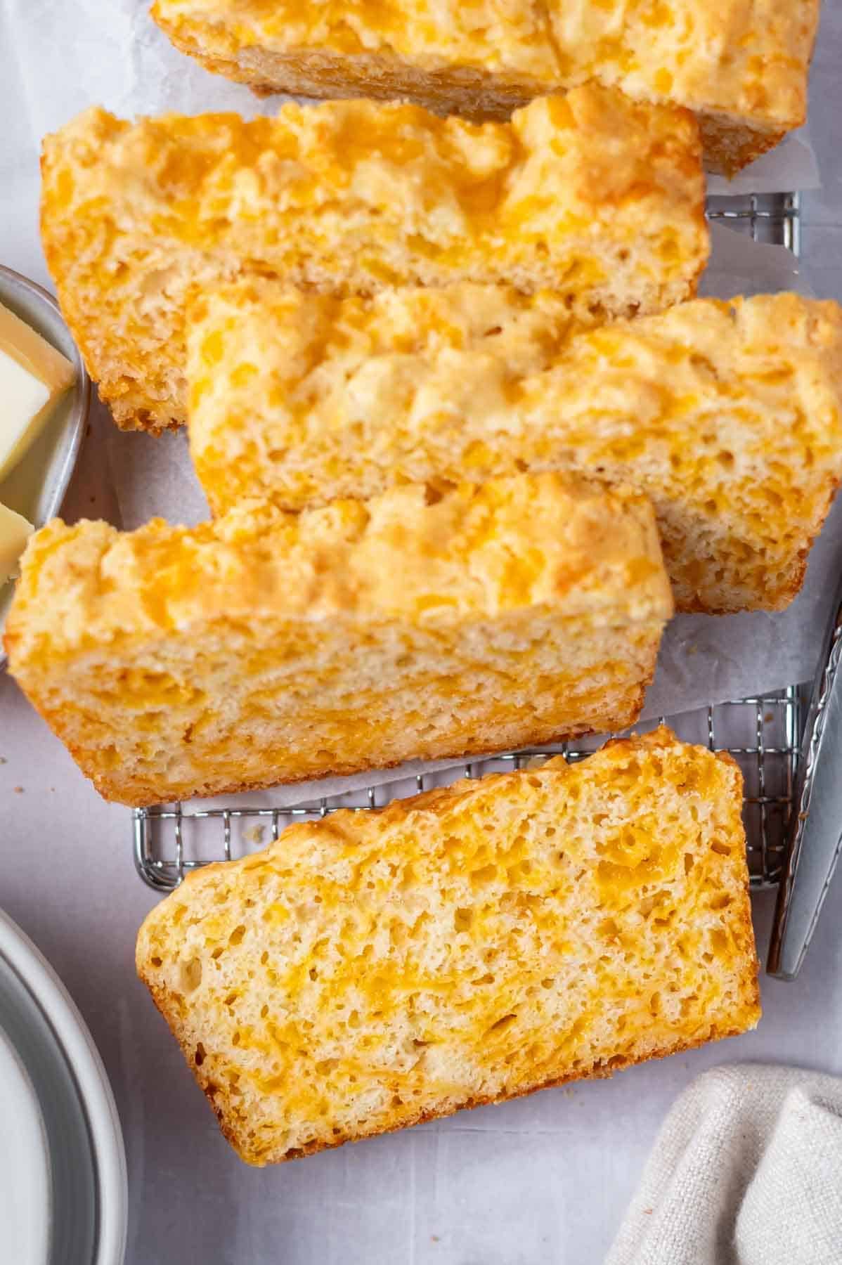 slices of cheese bread on a cooling rack with plates and butter on the side.