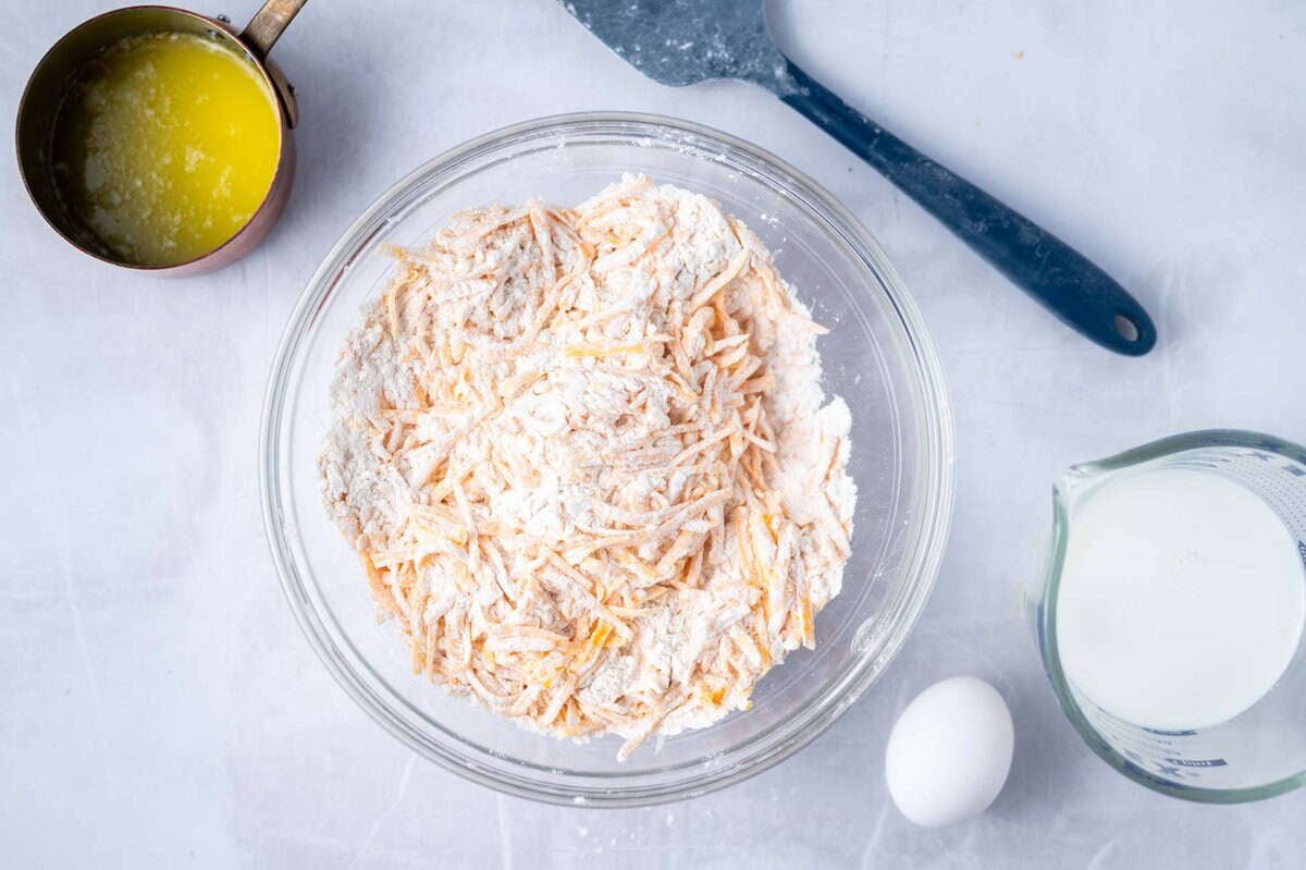 dry ingredients tossed with cheddar cheese in a mixing bowl
