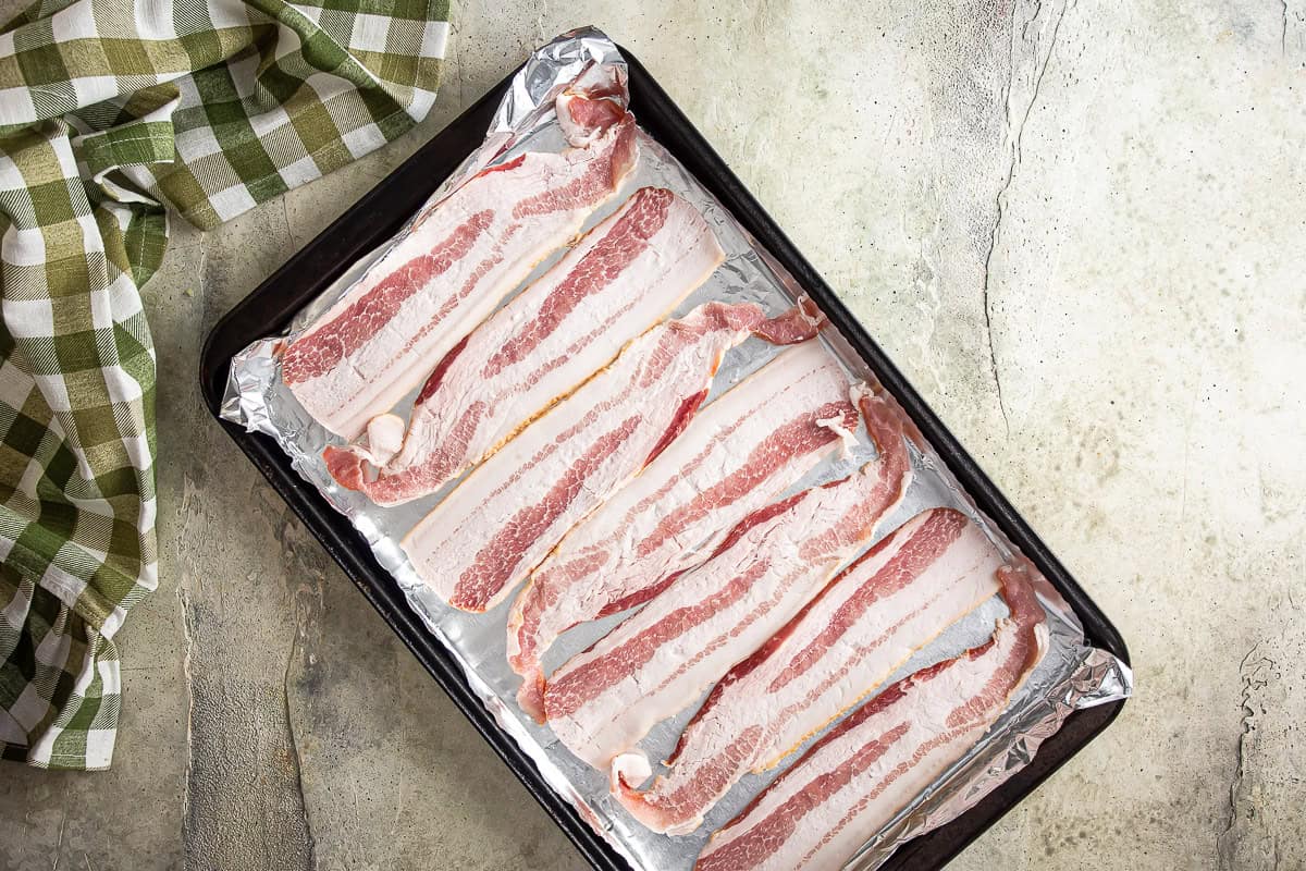 Bacon on a lined baking sheet before being partially cooked for jalapeno popper pizza.