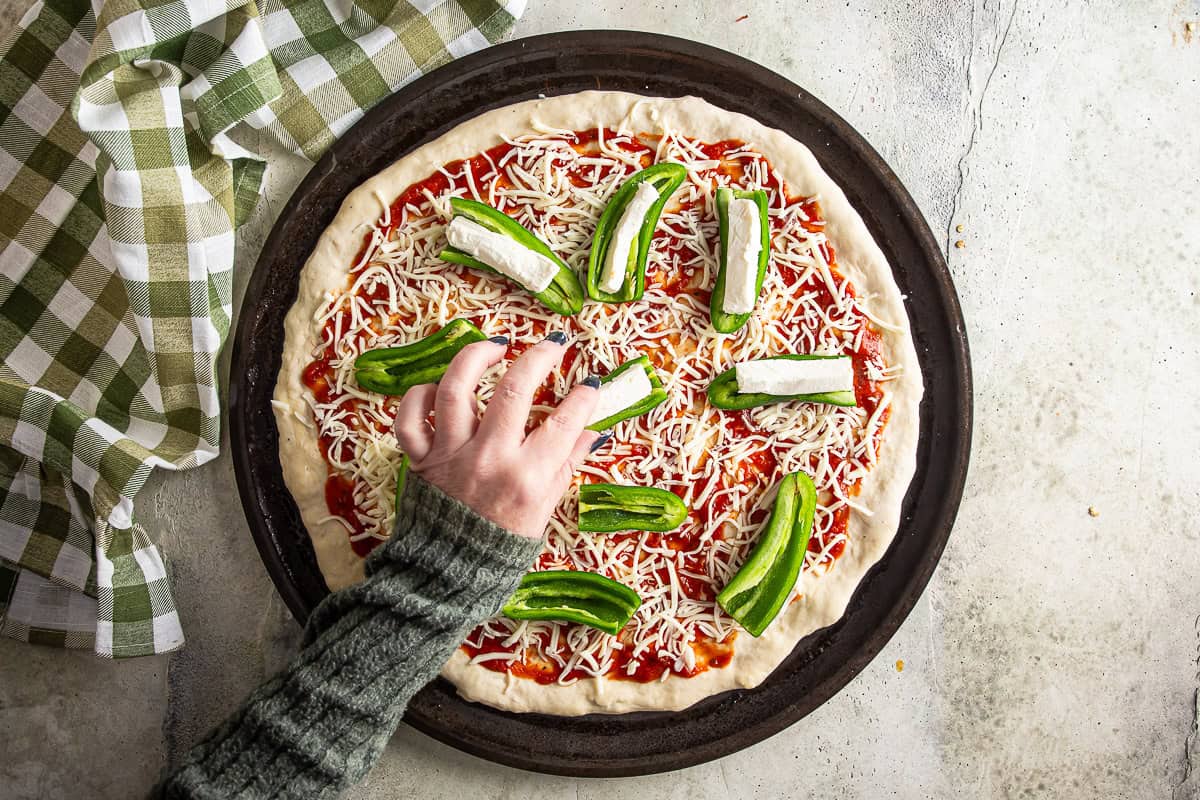 Adding cream cheese stuffed jalapenos to the top of the pizza.