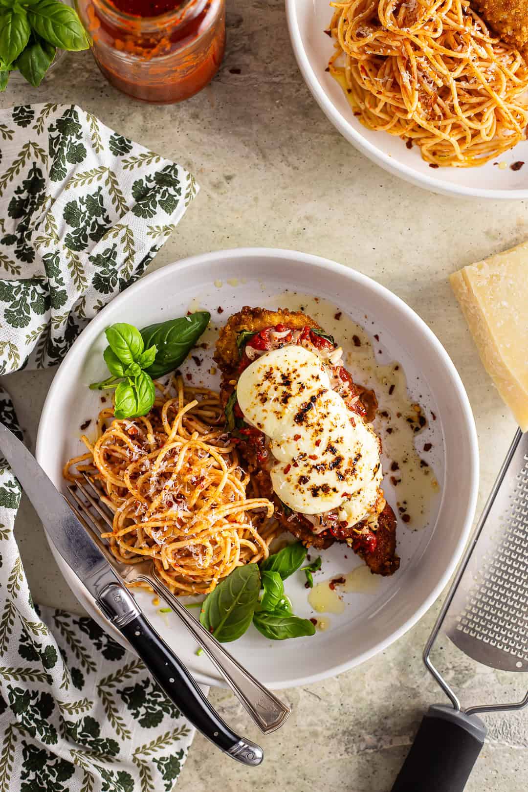 Chicken parmesan with pasta and fresh basil in a large, shallow white bowl.