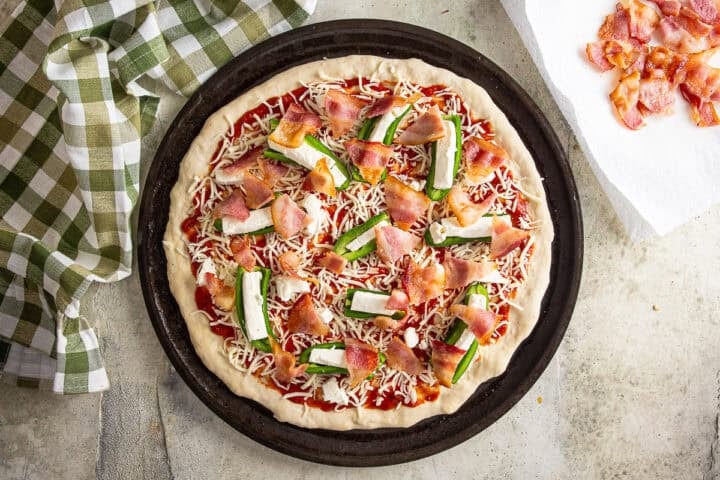 Layering par-cooked bacon onto the top of the pizza before being baked.