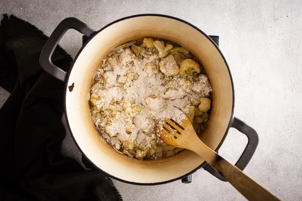 Adding flour to the cauliflower soup mixture to form a roux.
