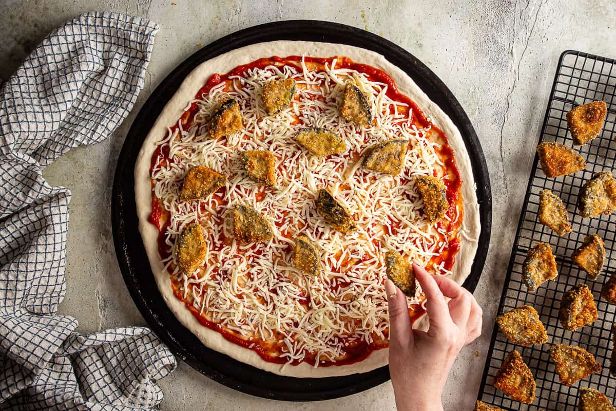 Topping a pizza with fried pieces of breaded eggplant.