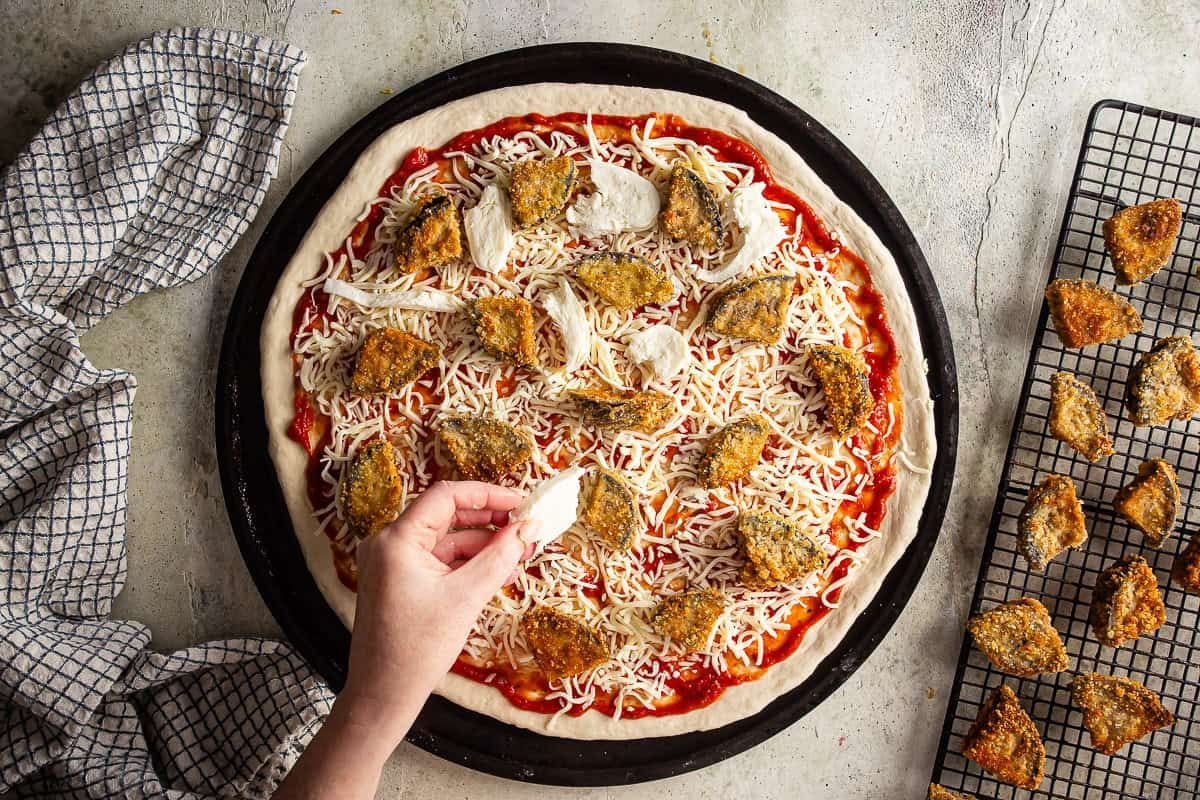 Adding fresh mozzarella to an eggplant parmesan pizza.