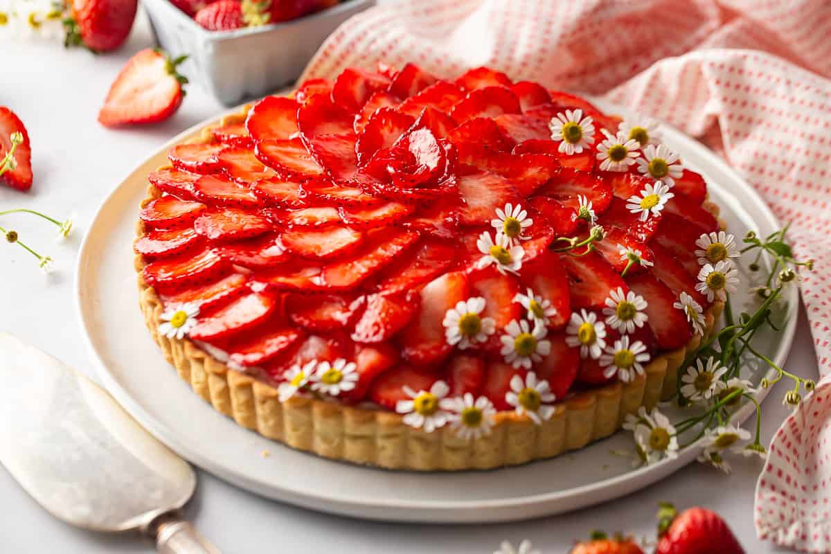 Strawberry tart on a decorated table with fresh strawberries in the background.