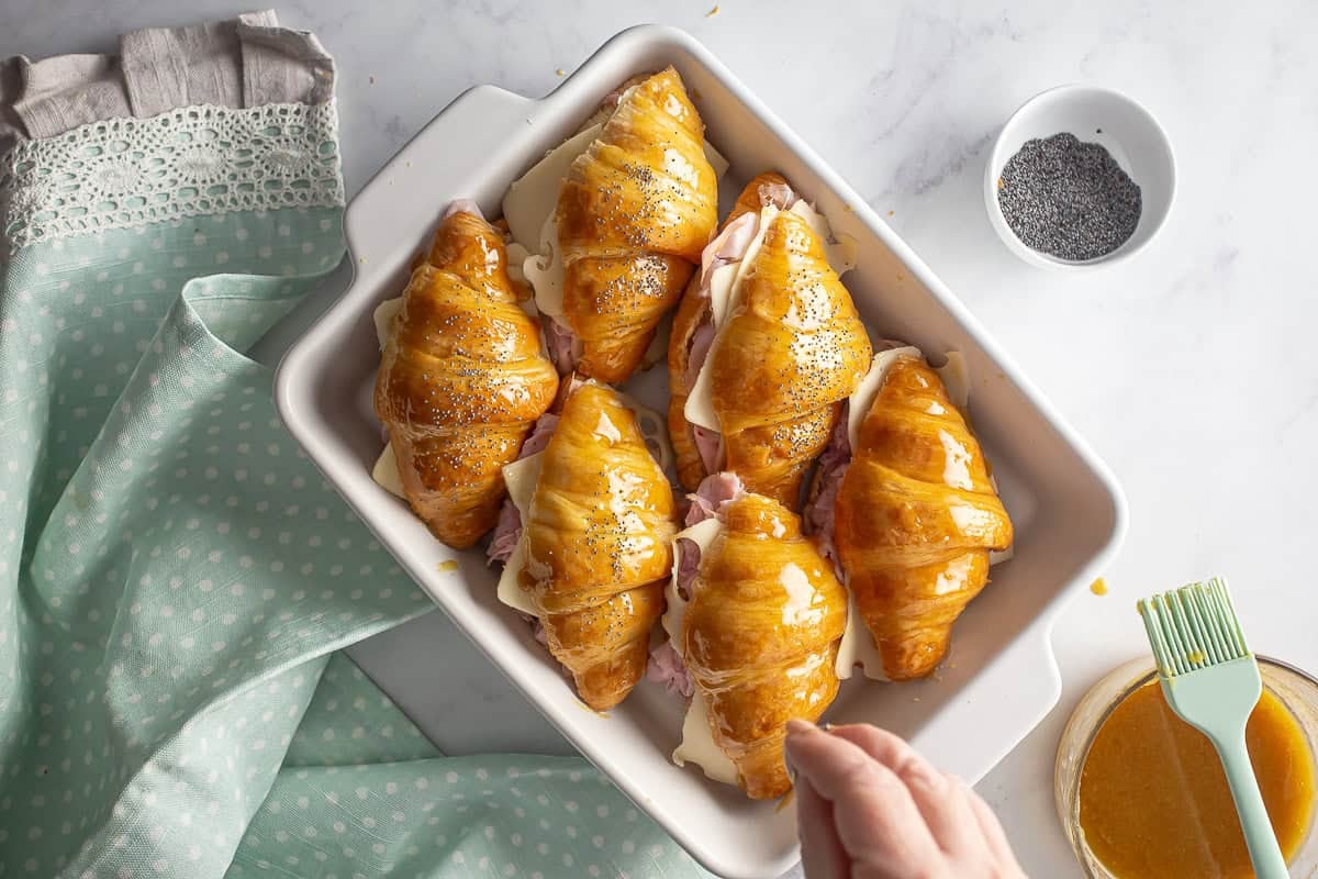 Poppy seeds being sprinkled on top of the glazed ham and cheese croissant sandwiches.