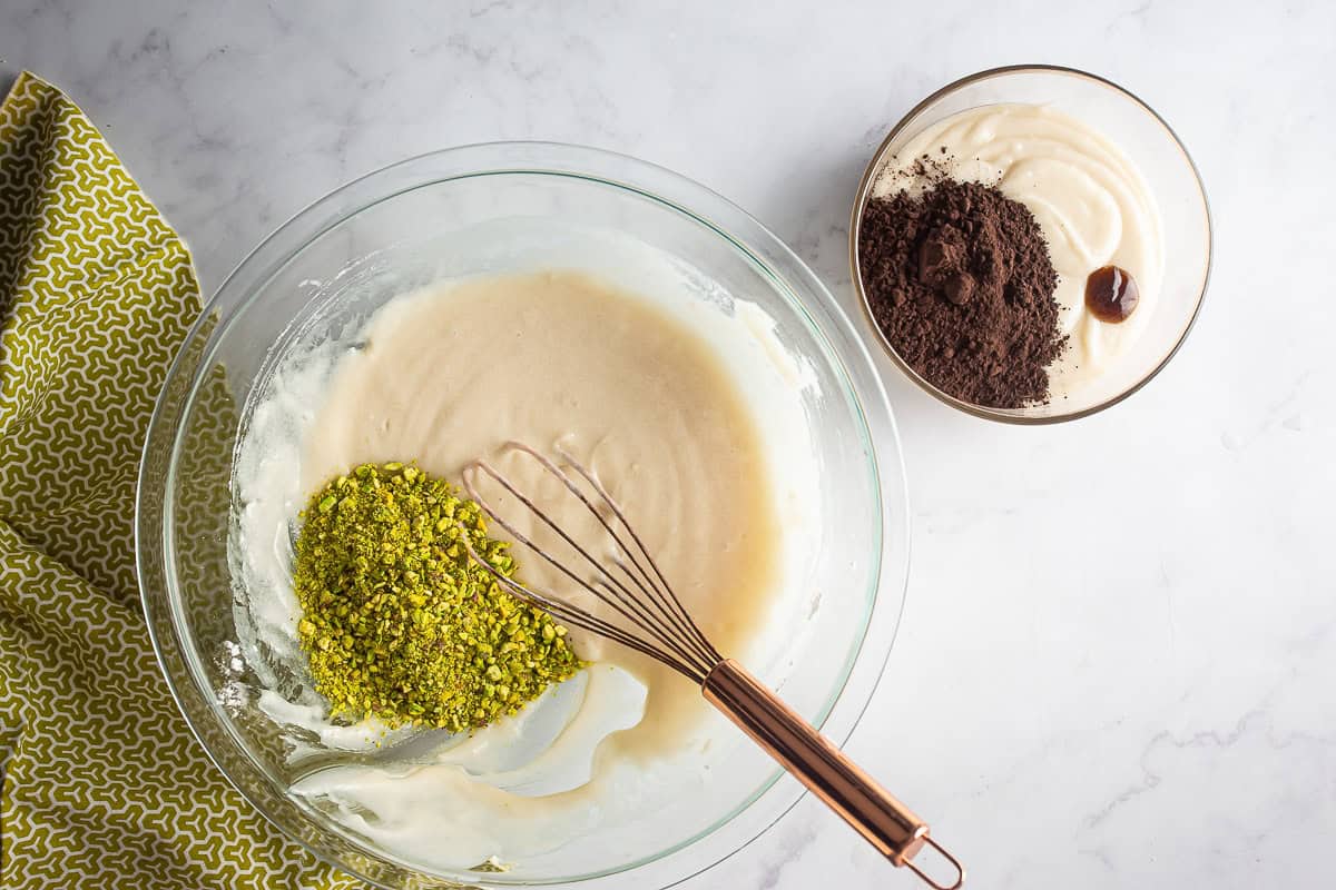 Batter for chocolate pistachio loaf split into two bowls with pistachio and cocoa added before being whisked.