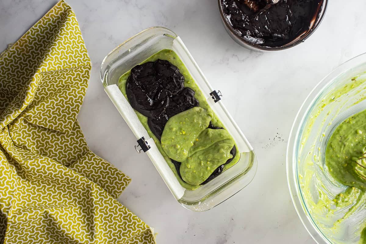 Batter for chocolate pistachio loaf being layered into a prepared loaf pan.