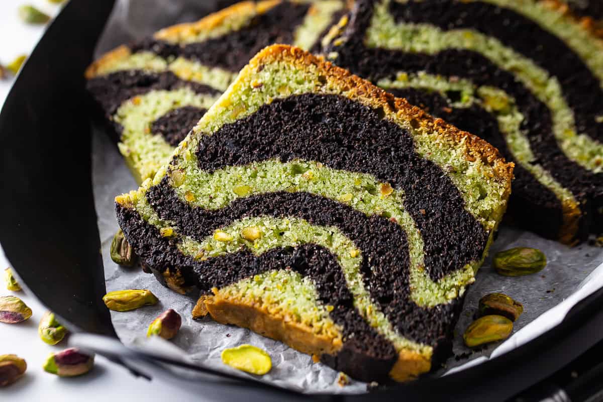 A close-up of a slice of pistachio cake on a plate with more pistachios.