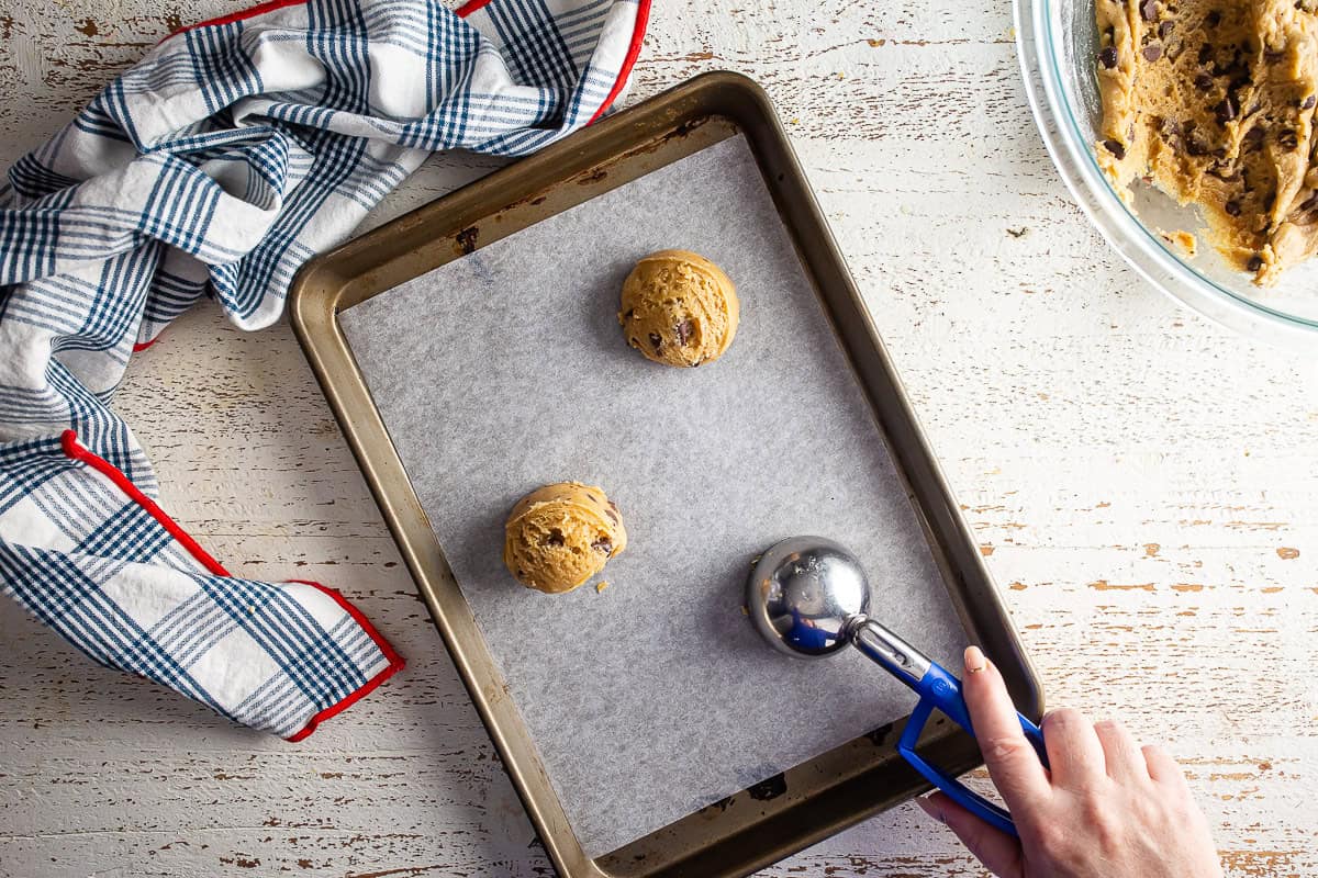 Scoops of cookie dough being placed onto a parchment-lined baking sheet.