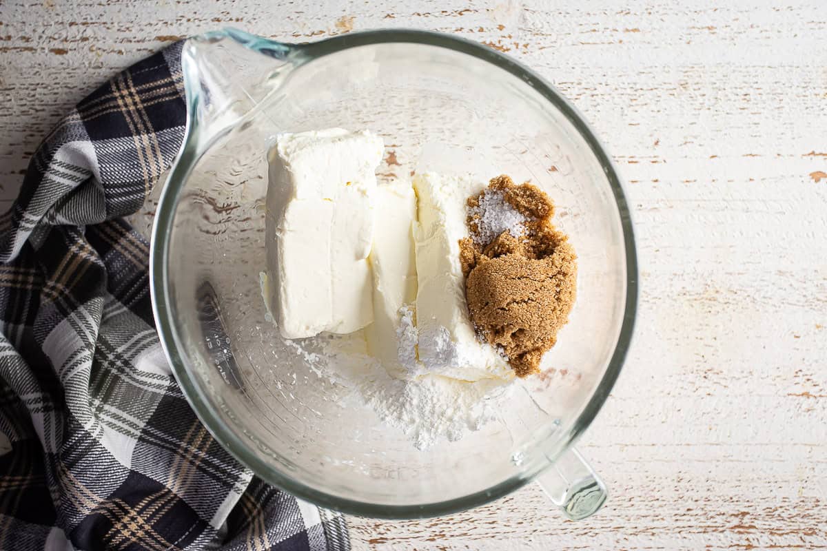 Cream cheese and sugars in the bowl of a mixer before being mixed.