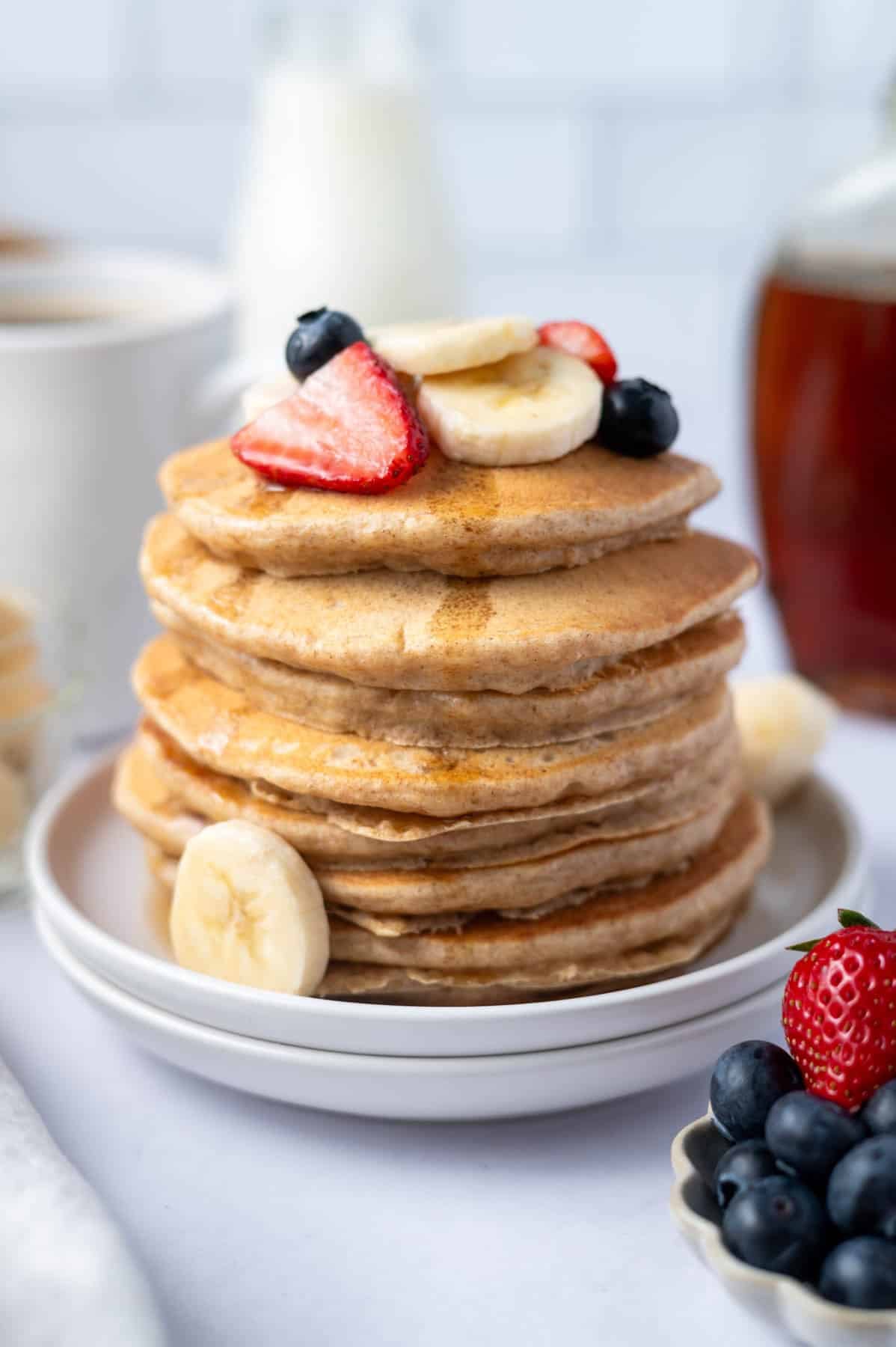 stack of pancakes with fresh fruit on top and syrup running down the sides