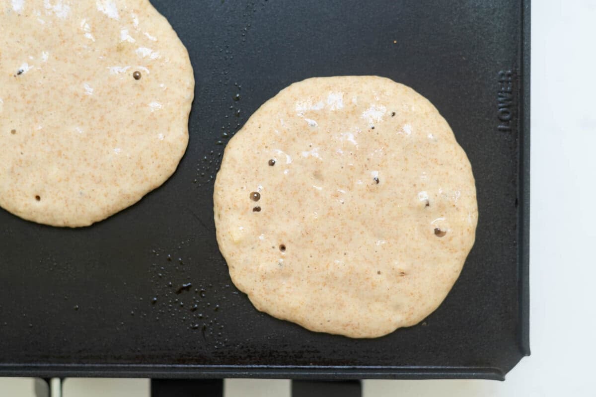 pancake batter on a griddle with large bubbles on the batter