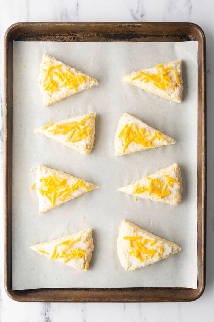 Scones on baking sheet topped with cheese