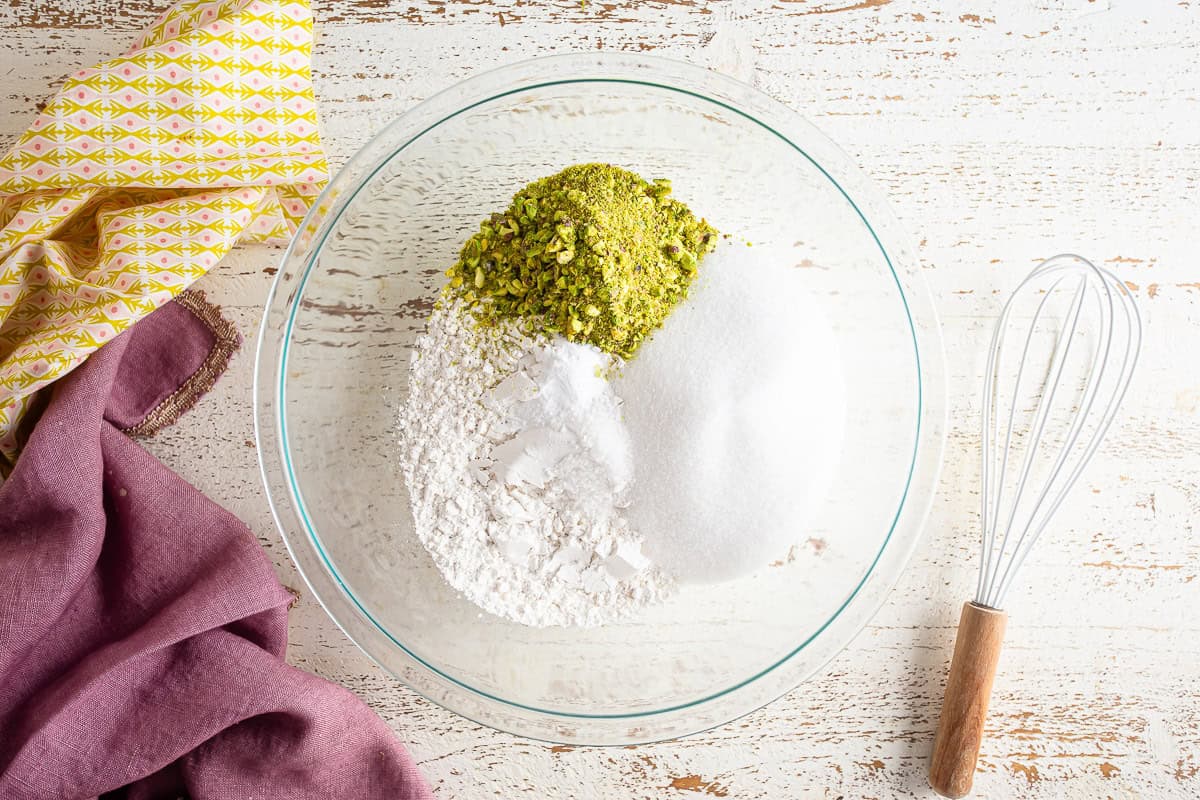 Dry ingredients for pistachio cake in a glass mixing bowl before being combined.