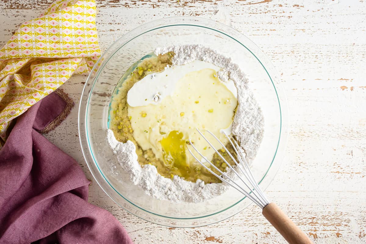 Wet ingredients being added to the dry ingredients for pistachio cake.