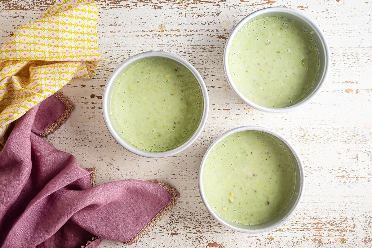 Pistachio cake batter in three prepared cake pans before being baked.