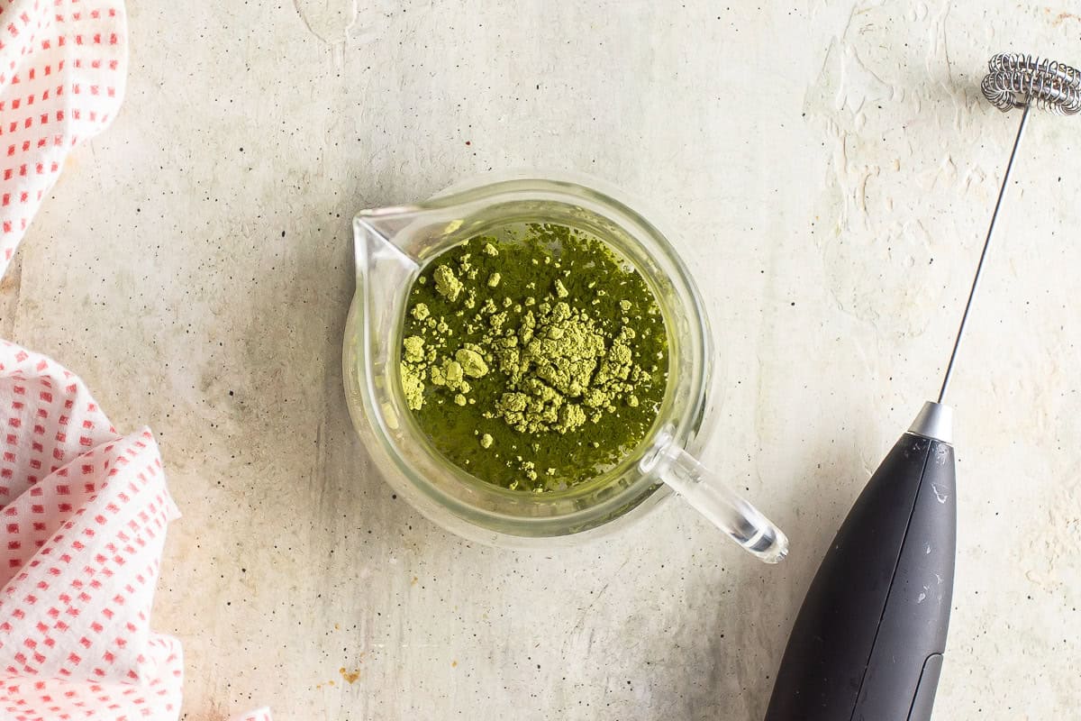 Hot water and matcha powder being blended for a matcha latte.