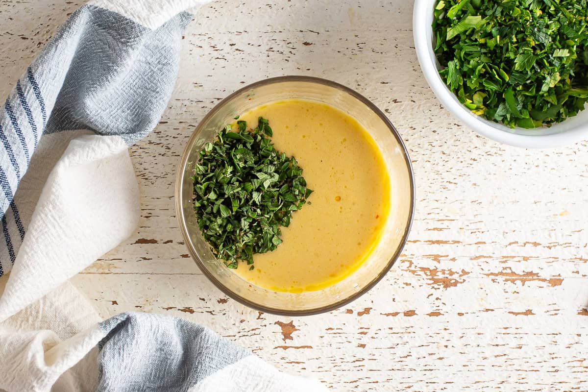 Adding fresh herbs to the emulsified oil and vinegar mixture for chimichurri.